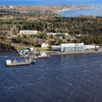 Une vue aérienne de la Station biologique de Saint Andrews au bord de l’eau et la ville de Saint Andrews en arrière-plan. Un groupe de neuf bâtiments, dont un grand édifice blanc sur la rive.