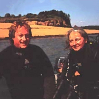 Une photo de Michael Strong et Maria Ines-Buzeta sur un bateau avec la berge et une plage de sable en arrière-plan.
